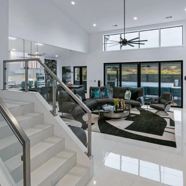 Two-story living room with glass-rail staircase and black area rug in Urban Oasis, a custom home by Mike Stevens Homes