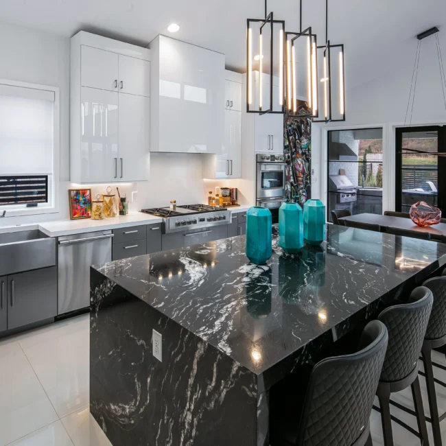 Kitchen with black waterfall-edge island, teal vases and stainless appliances in Urban Oasis by Mike Stevens Homes