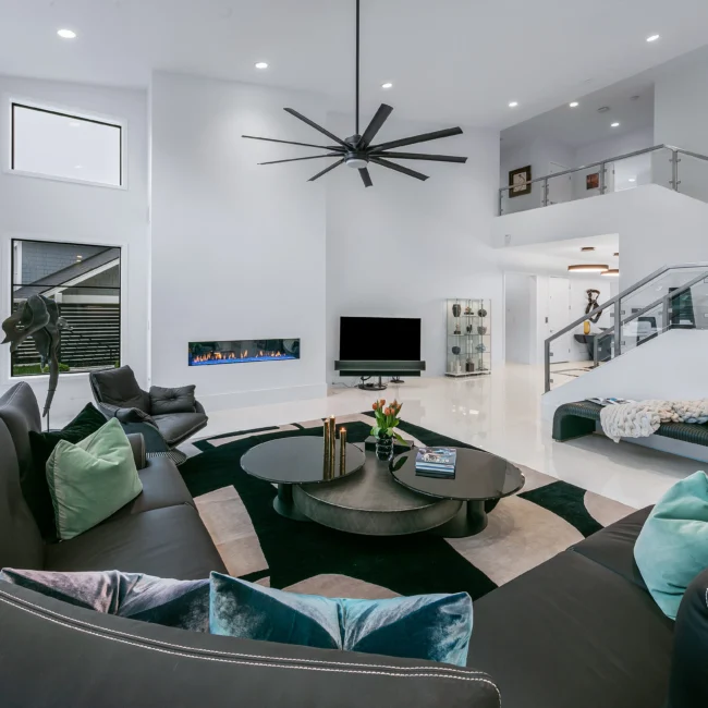 Great room with ceiling fan, black sectional and linear fireplace in Urban Oasis by Mike Stevens Homes