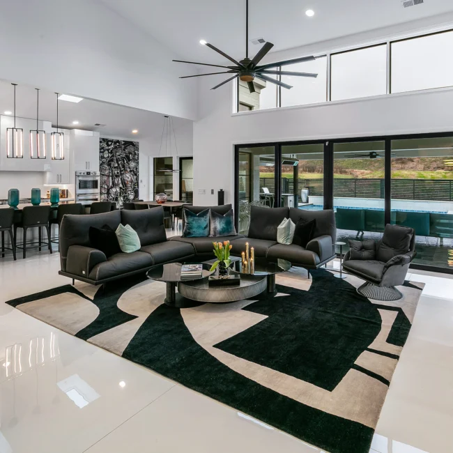 Great room with black-and-white rug, dark sectional and ceiling fan in Urban Oasis by Mike Stevens Homes