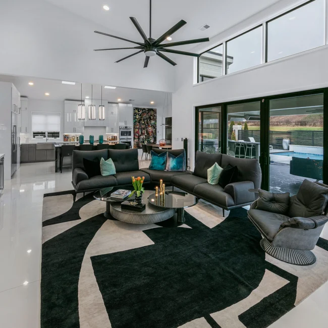 Living room with black sectional, oversized ceiling fan and patio doors in Urban Oasis by Mike Stevens Homes