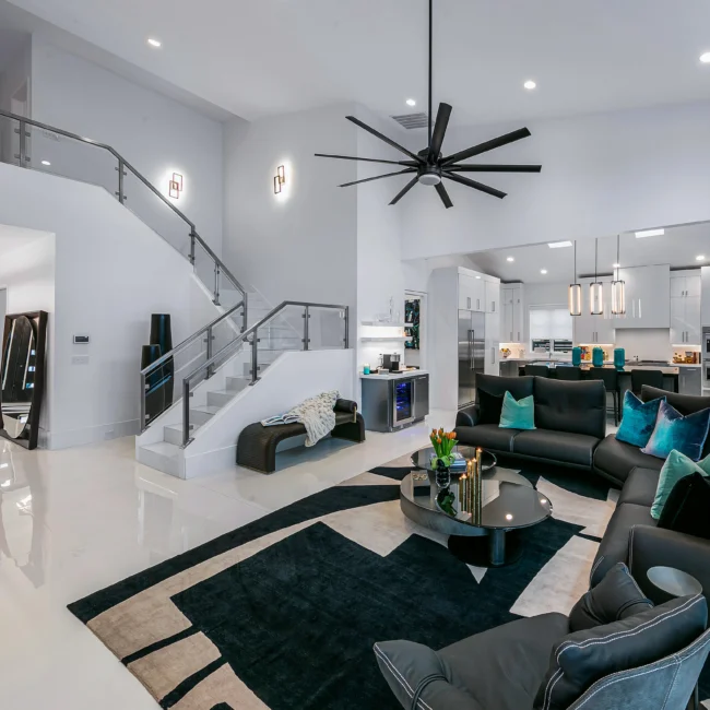 Living room with curved staircase, dark sectional and marble-look rug in Urban Oasis by Mike Stevens Homes