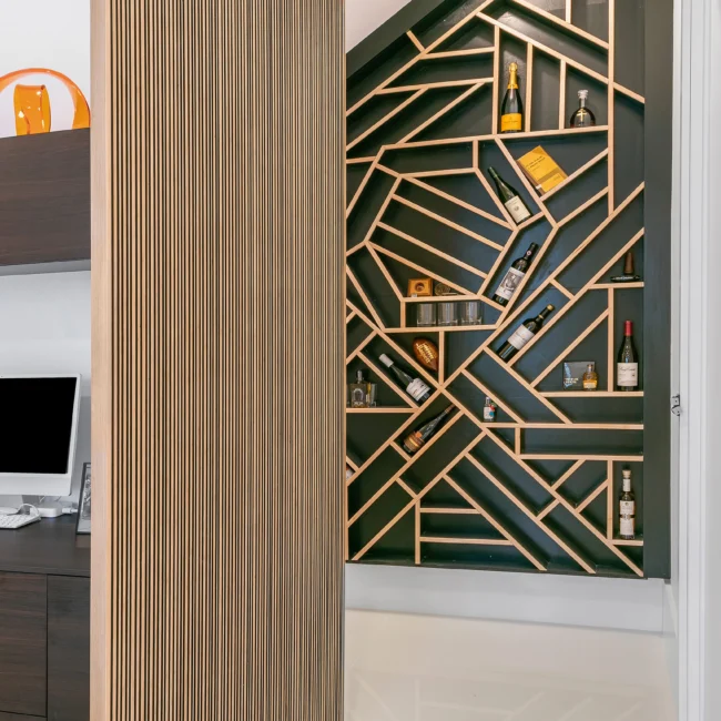 Vertical wood slat wall beside gold-lined geometric wine display niche in Urban Oasis by Mike Stevens Homes