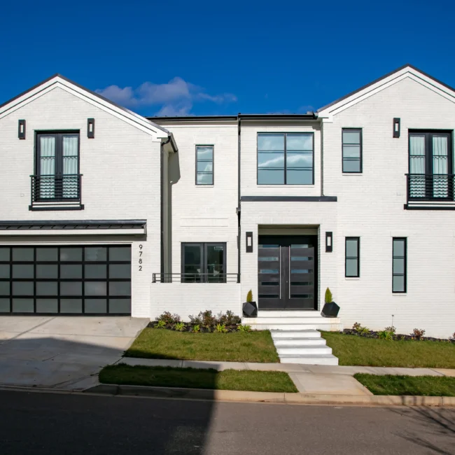 Front exterior of white brick two-story home with black-framed windows and covered entry in Urban Oasis by Mike Stevens Homes