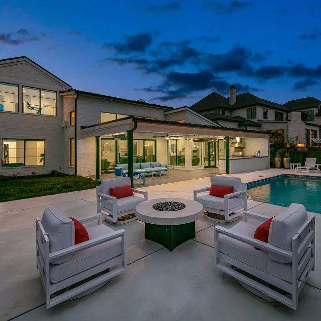 Patio at dusk with white lounge chairs, fire table and pool in Urban Oasis by Mike Stevens Homes