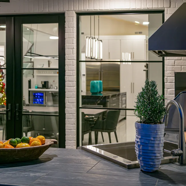 Kitchen seen through glass doors beside a bowl of citrus and tall planter in Urban Oasis by Mike Stevens Homes