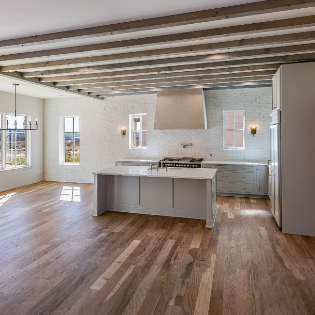 Kitchen with exposed beams, gray island and white brick in Minimalist French Farmhouse, a custom home by Mike Stevens Homes