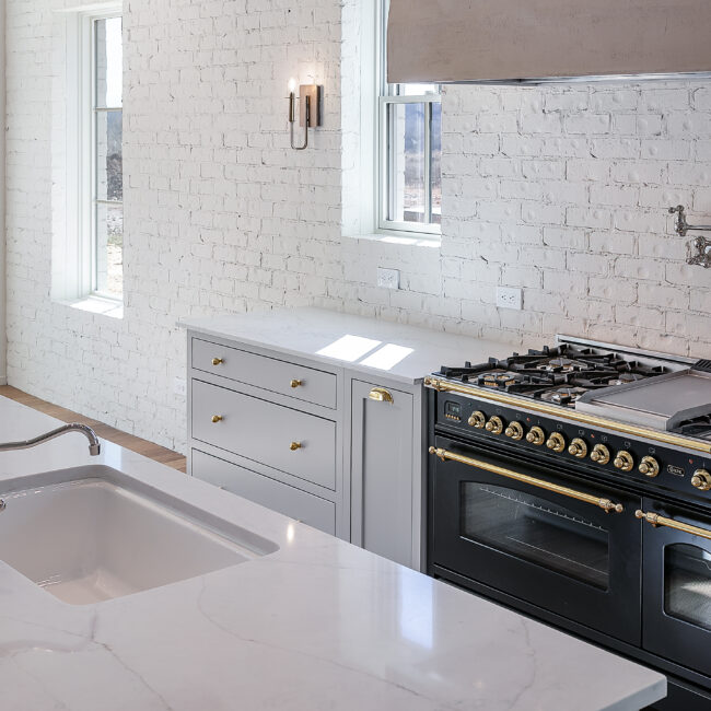 Gray cabinets beside a black range with brass trim in Minimalist French Farmhouse, a custom home by Mike Stevens Homes