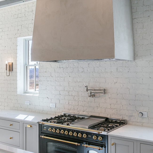 Black range with brass knobs and white brick backsplash in Minimalist French Farmhouse, a custom home by Mike Stevens Homes