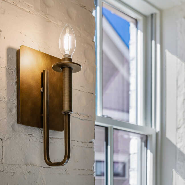 Brass wall sconce on white brick beside a window in Minimalist French Farmhouse, a custom home by Mike Stevens Homes