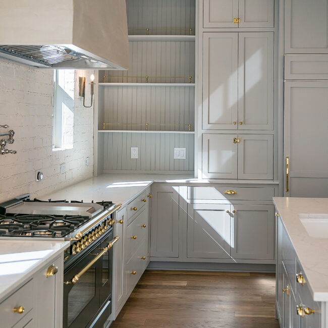 Gray cabinetry with open shelves and brass range in Minimalist French Farmhouse, a custom home by Mike Stevens Homes