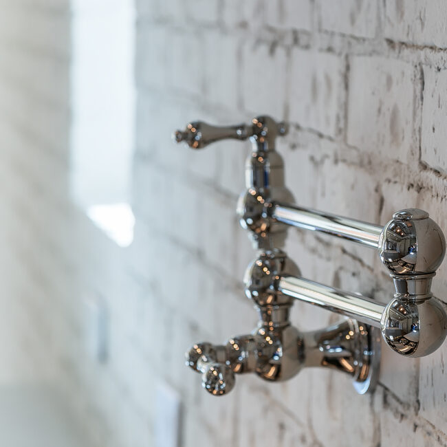 Close-up of chrome wall-mounted faucet on brick wall in Minimalist French Farmhouse, a custom home by Mike Stevens Homes