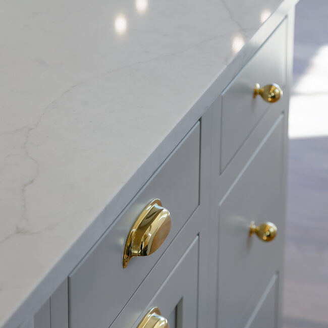 Quartz countertop with brass pull on gray cabinet in Minimalist French Farmhouse, a custom home by Mike Stevens Homes
