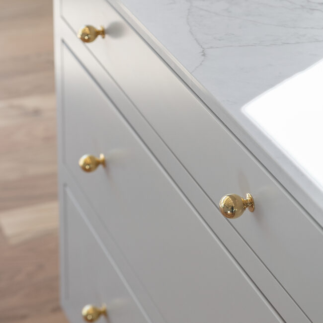 Close-up of brass knobs on gray drawer fronts in Minimalist French Farmhouse, a custom home by Mike Stevens Homes