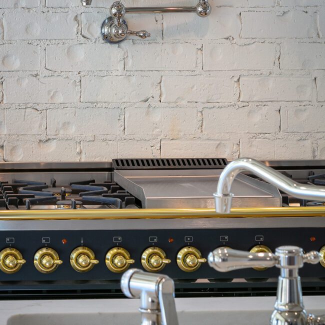 Range with brass trim, gas burners and polished faucet in Minimalist French Farmhouse, a custom home by Mike Stevens Homes