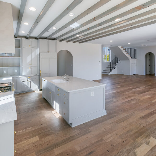 Open kitchen with arched doorways and white island in Minimalist French Farmhouse, a custom home by Mike Stevens Homes