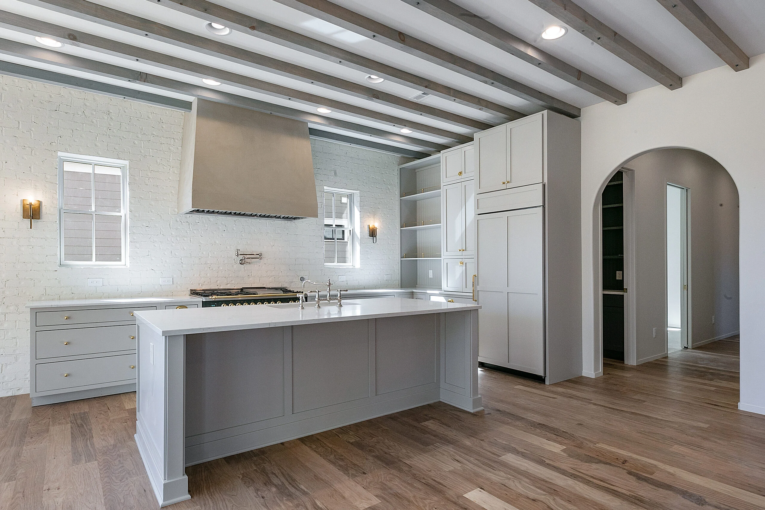 Gray kitchen island with cooktop under plaster hood in Minimalist French Farmhouse, a custom home by Mike Stevens Homes