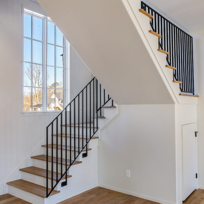 Staircase with black iron balusters and wood treads in Minimalist French Farmhouse, a custom home by Mike Stevens Homes