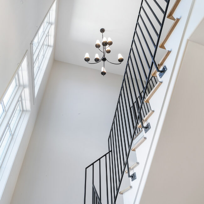 Stair landing with chandelier and black iron railing in Minimalist French Farmhouse, a custom home by Mike Stevens Homes