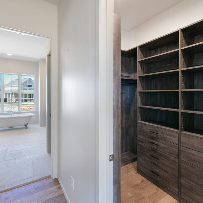 Walk-in closet with dark wood built-in shelving in Minimalist French Farmhouse, a custom home by Mike Stevens Homes