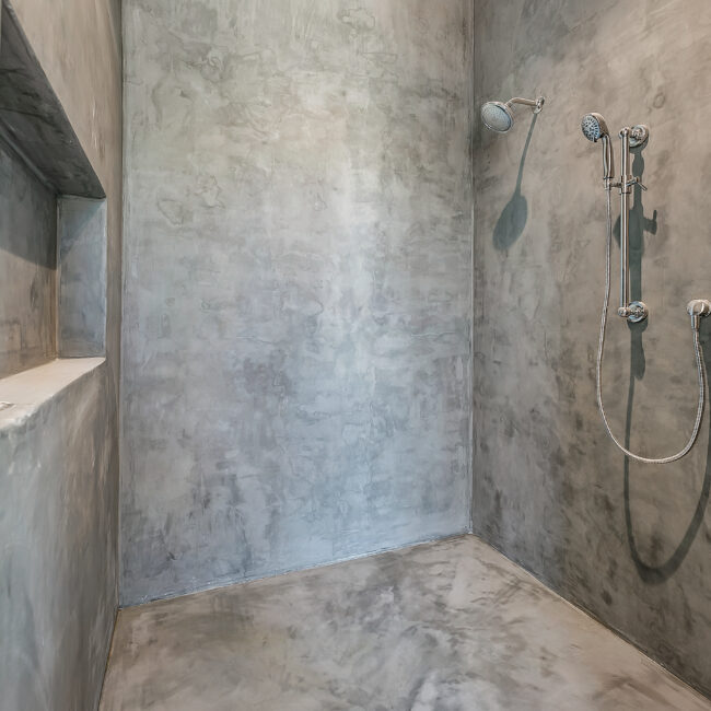 Walk-in shower with concrete walls and handheld wand in Minimalist French Farmhouse, a custom home by Mike Stevens Homes