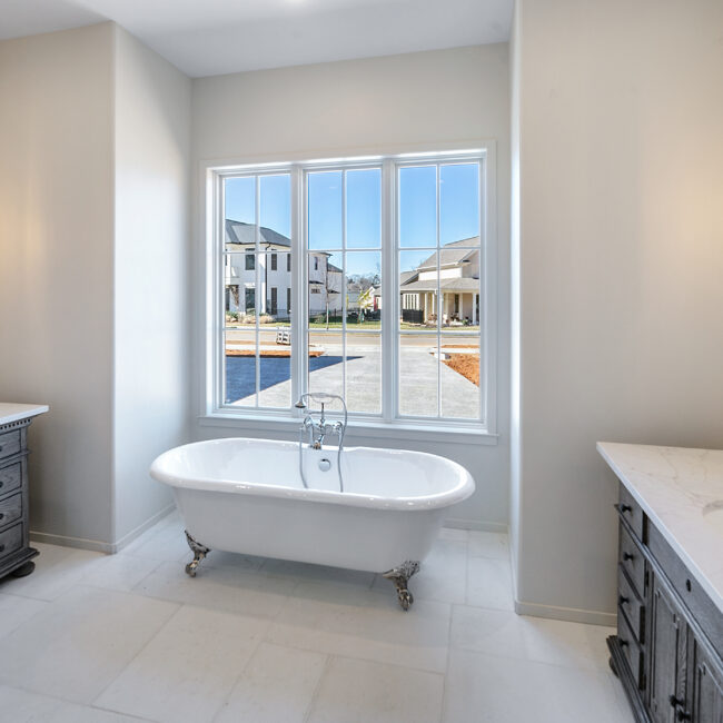 Clawfoot soaking tub under a bright window in Minimalist French Farmhouse, a custom home by Mike Stevens Homes