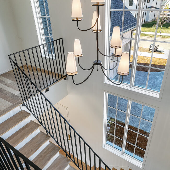 Staircase and chandelier beside two-story window in Minimalist French Farmhouse, a custom home by Mike Stevens Homes
