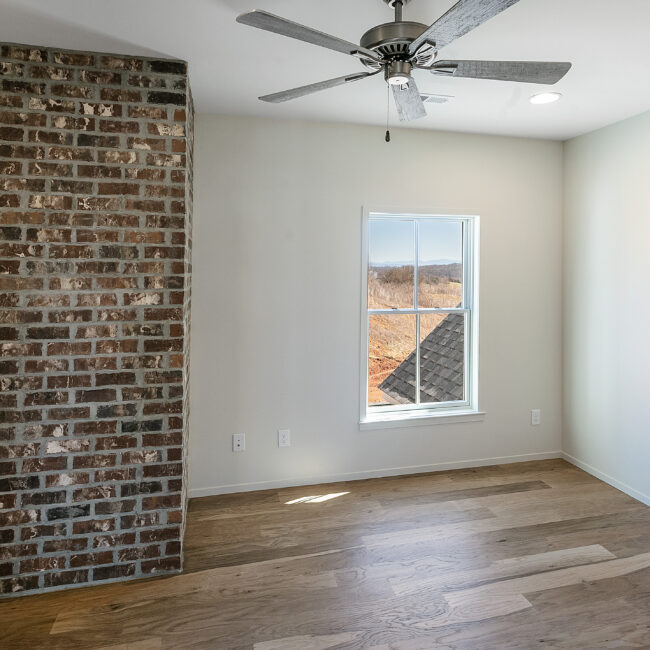 Bedroom with exposed brick wall and ceiling fan in Minimalist French Farmhouse, a custom home by Mike Stevens Homes