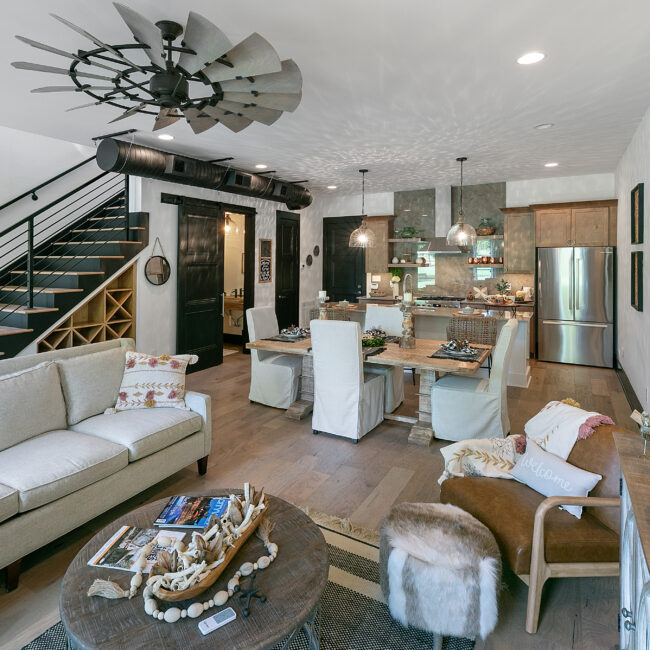 Living room with gray sofa, dark staircase and dining area in Urban Loft, a custom home by Mike Stevens Homes