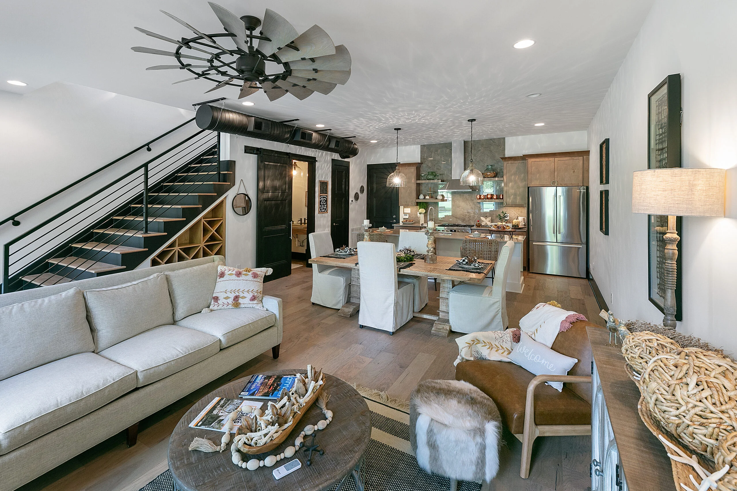 Living room with gray sofa, dark staircase and dining area in Urban Loft, a custom home by Mike Stevens Homes