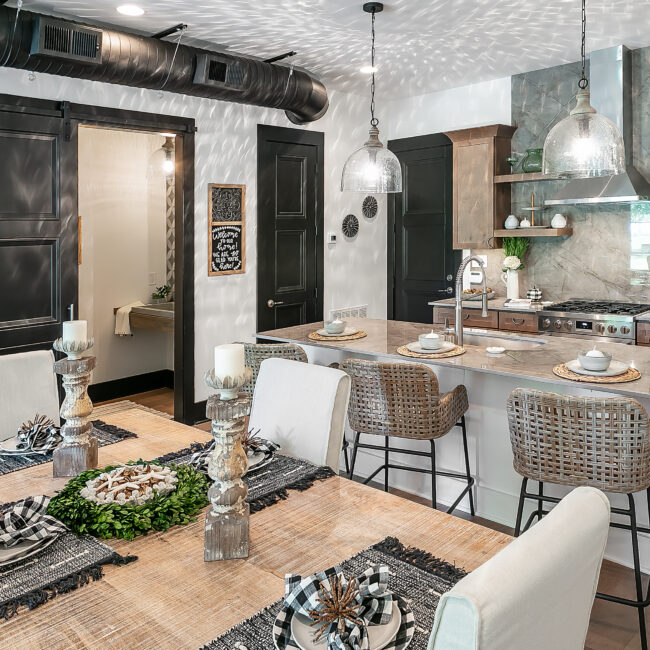 Kitchen island with wicker stools and dining table set for dinner in Urban Loft, a custom home by Mike Stevens Homes