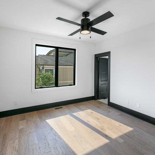 Bedroom with ceiling fan, black-framed window and wood floors in Urban Loft, a custom home by Mike Stevens Homes