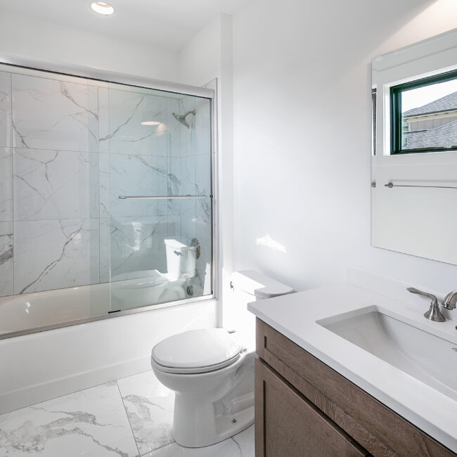 Bathroom with tub-shower, marble-look tile and white vanity in Urban Loft, a custom home by Mike Stevens Homes