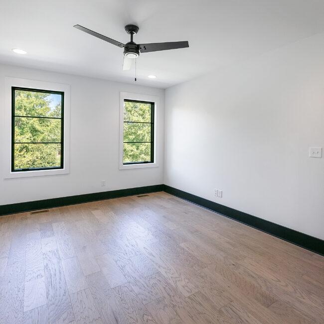 Empty bedroom with two windows and hardwood floors in Urban Loft, a custom home by Mike Stevens Homes