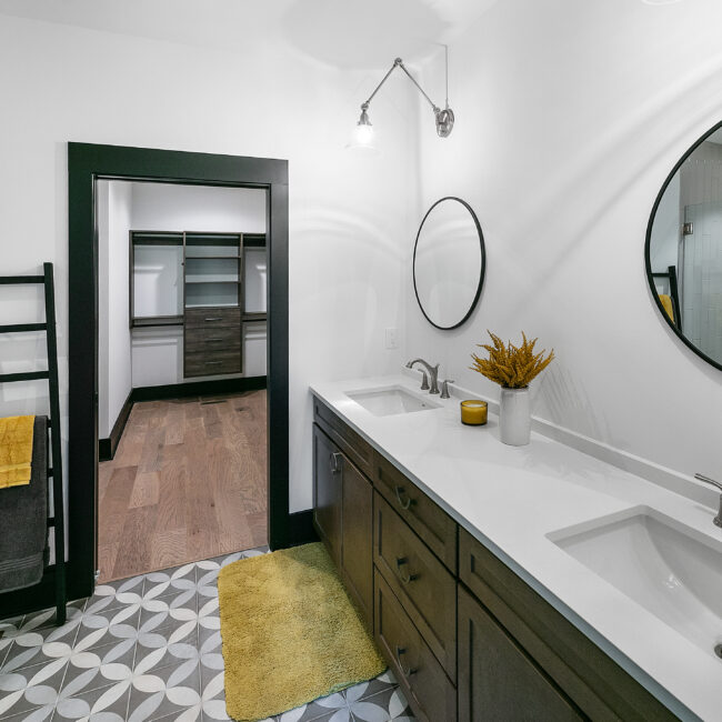 Bathroom with double sinks, round mirror and patterned floor tile in Urban Loft, a custom home by Mike Stevens Homes