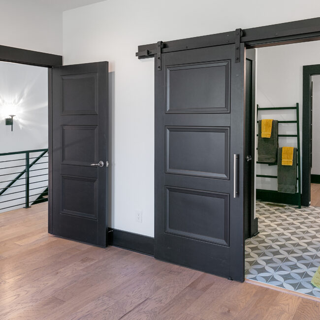 Black barn door opening to a hallway with towel ladder in Urban Loft, a custom home by Mike Stevens Homes