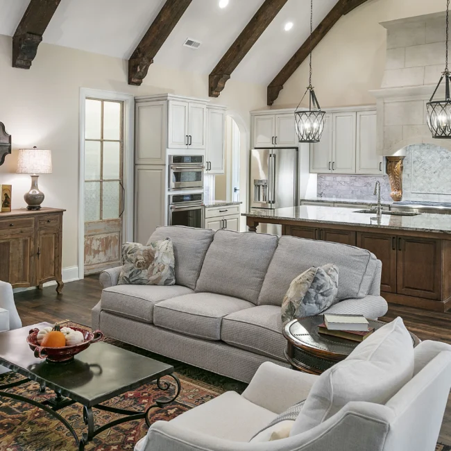 Family room with gray sofa, rug and cream kitchen beyond in European Villa, a custom home by Mike Stevens Homes