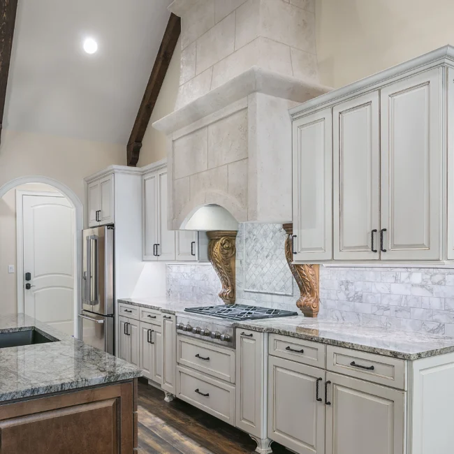 Cream kitchen with plaster range hood, marble backsplash and wall oven in European Villa, a custom home by Mike Stevens Homes