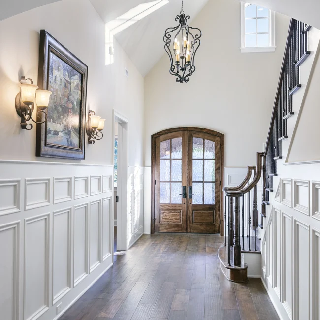 Entry foyer with arched wood door, wainscoting and iron chandelier in European Villa, a custom home by Mike Stevens Homes