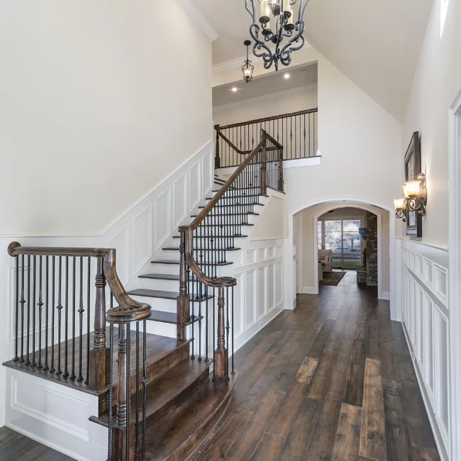 Wainscoted staircase with iron balusters under a chandelier in European Villa, a custom home by Mike Stevens Homes