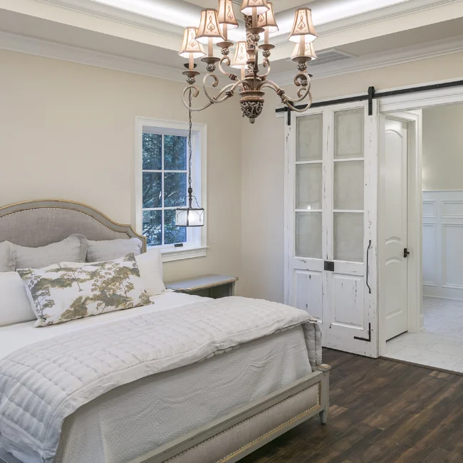 Primary bedroom with chandelier, barn door and white bedding in European Villa, a custom home by Mike Stevens Homes
