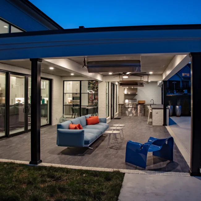 Covered patio with ceiling fan, blue chairs and outdoor kitchen in Urban Oasis by Mike Stevens Homes