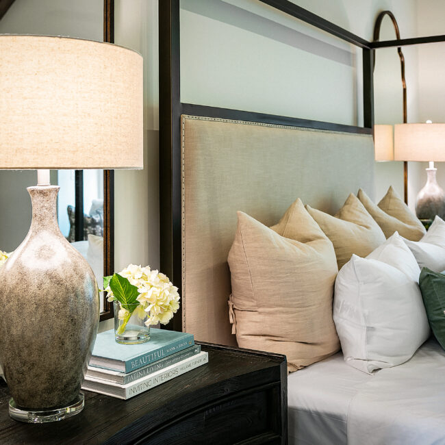 Bedside lamp, flowers and stacked books on nightstand in Southern Belle, a custom home by Mike Stevens Homes