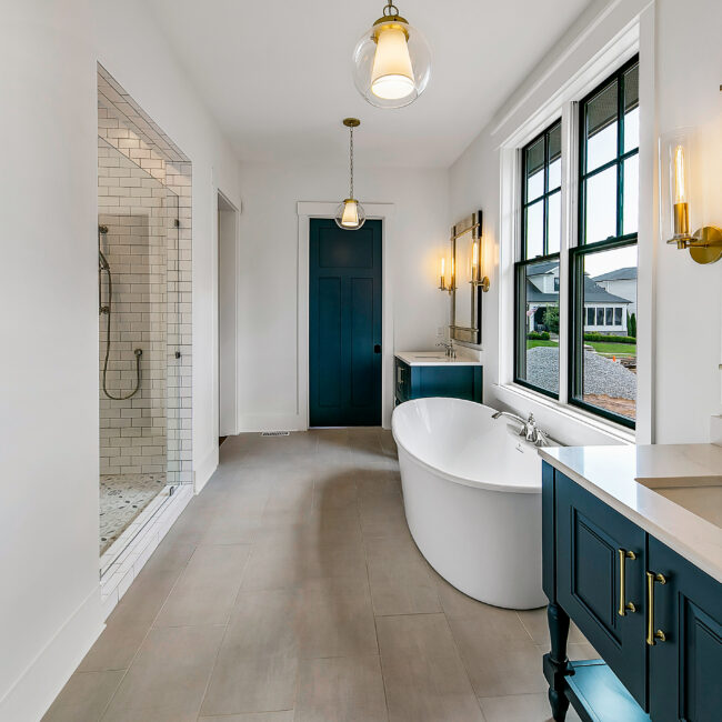 Freestanding white soaking tub beside navy vanity in primary bath in Southern Belle, a custom home by Mike Stevens Homes