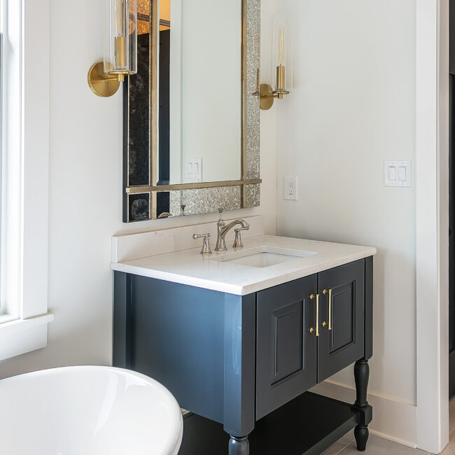 Navy bath vanity with brass faucet, arched mirror and sconce in Southern Belle, a custom home by Mike Stevens Homes
