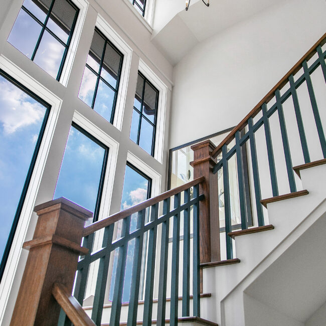 Staircase with wood newel and iron railing beside tall windows in Southern Belle, a custom home by Mike Stevens Homes
