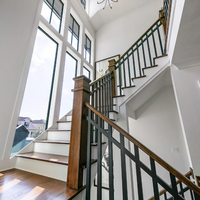 Staircase with iron balusters and wood handrail by a large window in Southern Belle, a custom home by Mike Stevens Homes
