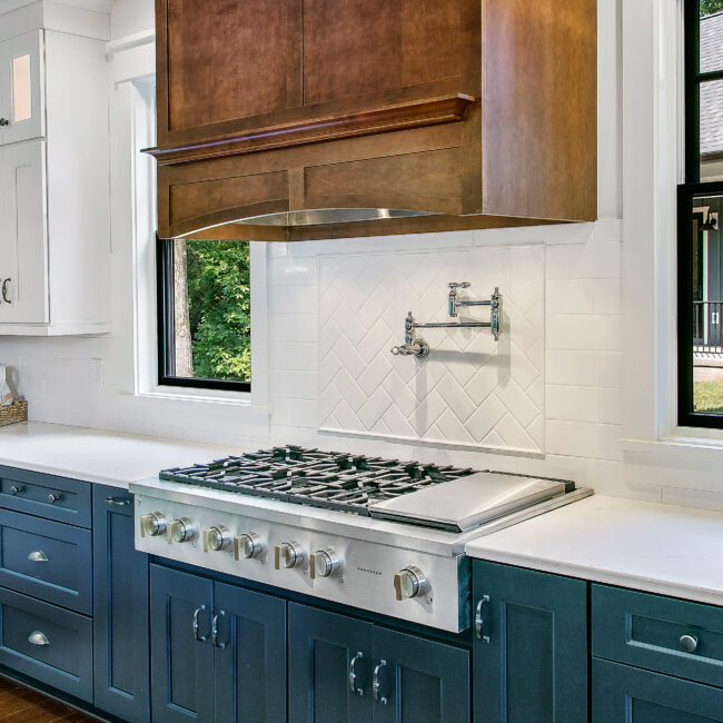 Kitchen range with pot filler above herringbone tile backsplash in Southern Belle, a custom home by Mike Stevens Homes