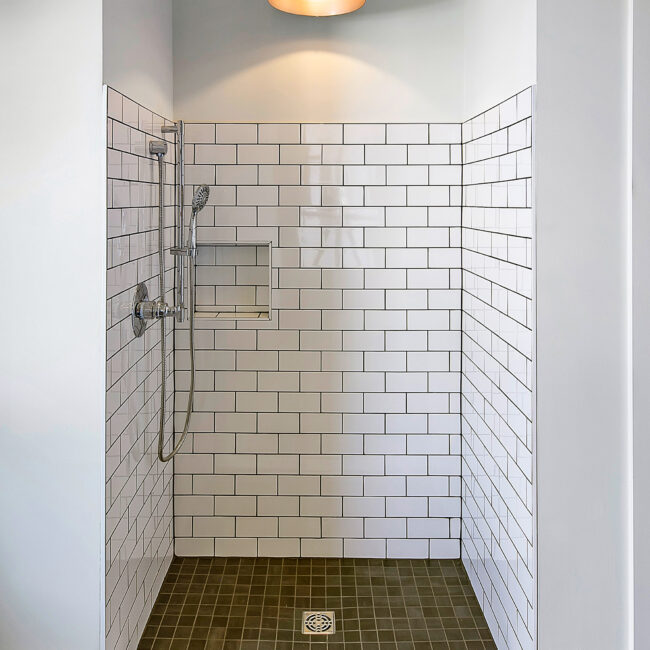 Walk-in shower with white subway tile and dark floor tile drain in Southern Belle, a custom home by Mike Stevens Homes