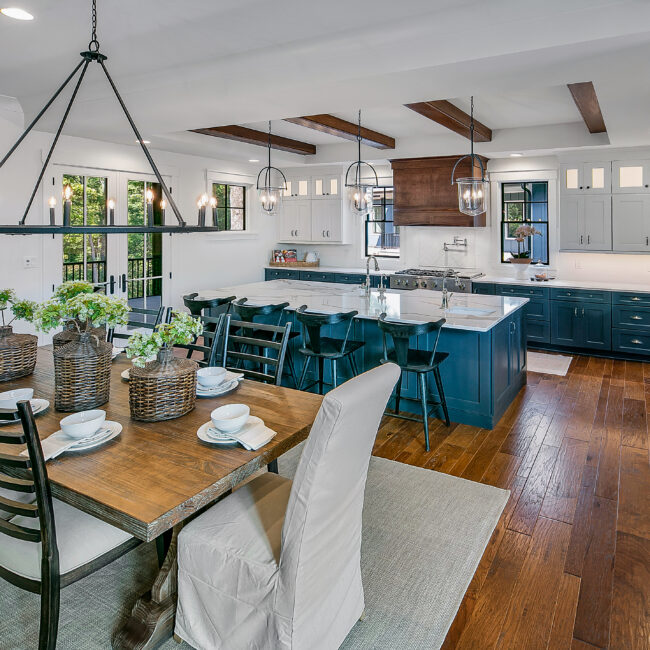 Wood dining table and slipcovered chairs beside teal kitchen island in Southern Belle, a custom home by Mike Stevens Homes